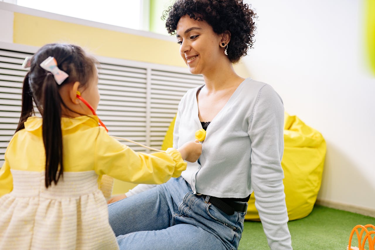 A child plays doctor with a stethoscope and a smiling adult indoors.